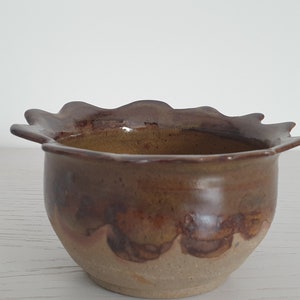 May include: A small, brown ceramic bowl with a scalloped rim. The bowl has a light brown glaze with darker brown accents.