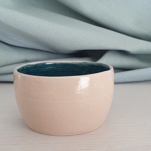 Può includere: Una piccola ciotola rotonda in ceramica con un esterno rosa chiaro e un interno blu turchese.