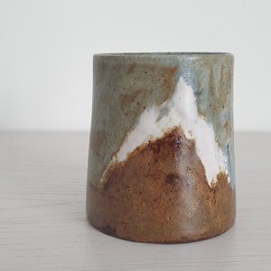 Peut inclure: Une tasse en céramique avec un glaçage brun, blanc et bleu. Le glaçage a un motif moucheté et abstrait.