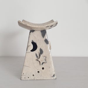 May include: A white ceramic incense burner with a black and white design. The burner has a crescent moon and a star cutout.