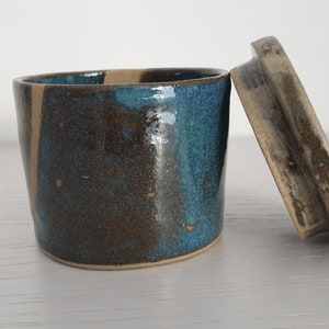 Peut inclure: Un petit pot à beurre en céramique avec un couvercle. Le pot est émaillé dans des tons de brun, bleu et beige. Le couvercle est également émaillé en brun et beige.