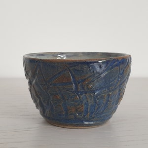 Könnte beinhalten: Eine kleine, blaue Keramikschüssel mit einem strukturierten, geprägten Design. Die Schüssel hat eine leicht abgerundete Form und eine glatte, glasierte Oberfläche.