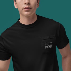 May include: Black t-shirt with a crew neck and short sleeves. A pocket on the left chest features the white text "USELESS POCKET". The shirt is made of a soft material and is suitable for casual wear.
