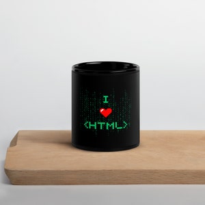 Puede incluir: Taza de café negra con un diseño pixelado verde y rojo que dice "I <3 HTML".
