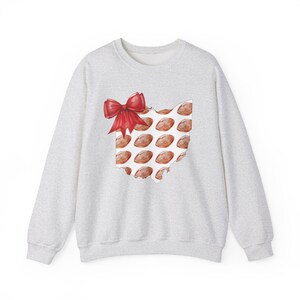 May include: A light gray sweatshirt featuring a red bow and a design of the state of Ohio filled with footballs. The footballs are brown with white laces. The bow is a bright red color.