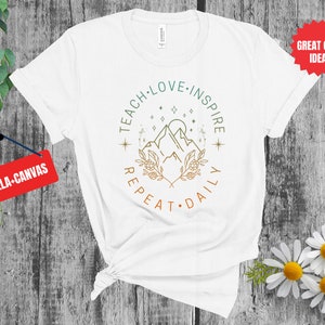 May include: White t-shirt with a green, brown, and orange graphic design that says "Teach Love Inspire Repeat Daily" with a mountain and stars in the center.