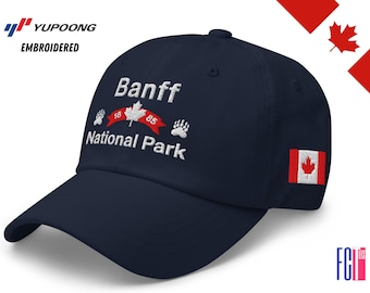 May include: Navy blue baseball cap embroidered with "Banff National Park" and a Canadian flag. The cap features a curved brim and a small Canadian flag patch on the side. The text includes the years "18" and "85".