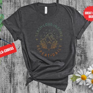 May include: A dark gray t-shirt with a graphic design of mountains, stars, and the text "Teach Love Inspire Repeat Daily".