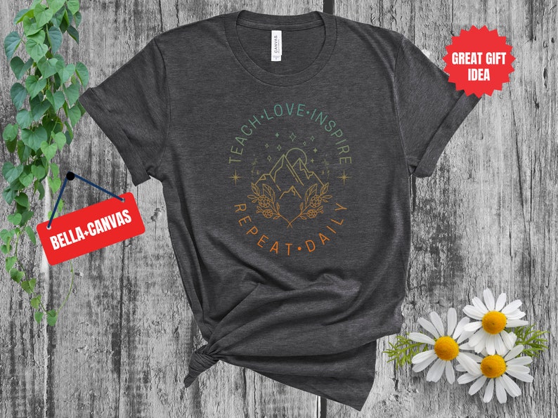 May include: A dark gray t-shirt with a graphic design of mountains, stars, and the text "Teach Love Inspire Repeat Daily".