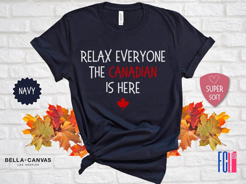 以下が含まれることがあります： 紺色のTシャツに、「リラックスみんなカナダ人はここにいる」という白い文字が書かれています。テキストの下には赤いカエデの葉があります。