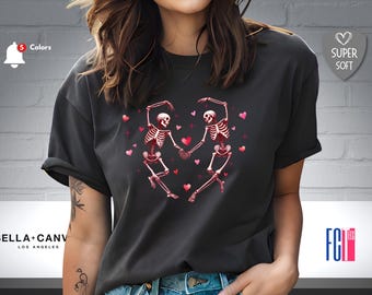 May include: Black t-shirt with a graphic of two skeletons dancing with hearts. The skeletons are pink and white, and the hearts are red.