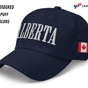 May include: A navy blue baseball cap with a white embroidered "ALBERTA" on the front and a small Canadian flag on the side. The cap is made of a soft, comfortable material and has a 3D puff embroidery.