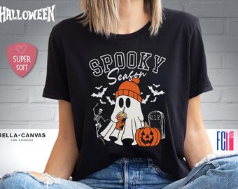May include: Black t-shirt featuring a white ghost holding a drink and the text "Spooky Season". There is a pumpkin and a tombstone with the text "RIP" on it.