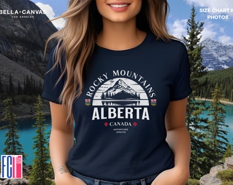 May include: A navy blue t-shirt featuring a white graphic of a mountain range and the text "Rocky Mountains Alberta Canada Adventure Awaits".