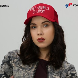 Puede incluir: Una gorra de b&eacute;isbol roja con el texto "MAKE AMERICA GO AWAY" bordado en blanco. La gorra la lleva puesta una persona con el pelo largo y oscuro.
