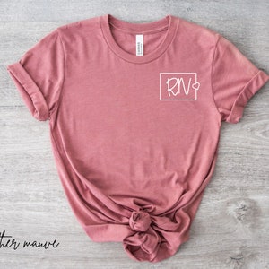 May include: Heather mauve t-shirt with a white graphic of a square containing the letters "RN" and a small heart.
