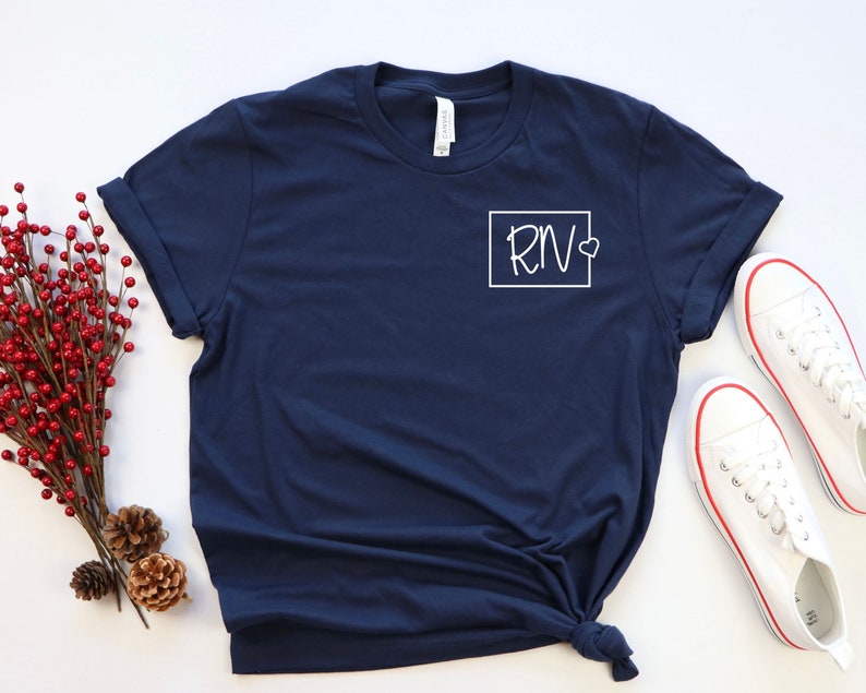 May include: A navy blue t-shirt with a white square on the left chest that says "RN" with a small heart next to the "N".