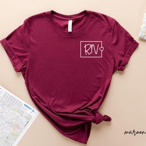 May include: Maroon t-shirt with a white square graphic that says "RN" with a small heart next to it.