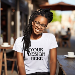 Könnte beinhalten: Ein weißes T-Shirt mit dem Text "YOUR DESIGN HERE" auf der Vorderseite. Das Shirt wird von einer Person mit langen schwarzen Dreadlocks und Brille getragen.