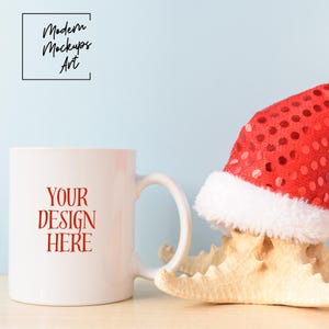 Könnte beinhalten: Eine weiße Keramiktasse mit dem roten Text "YOUR DESIGN HERE" auf der Vorderseite. Die Tasse steht neben einem Seestern, der einen roten und weißen Weihnachtsmann-Hut trägt.