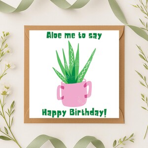 May include: A square greeting card with a brown border features a green aloe vera plant in a pink pot. The text "Aloe me to say" and "Happy Birthday!" are in green. The card is surrounded by decorative greenery.