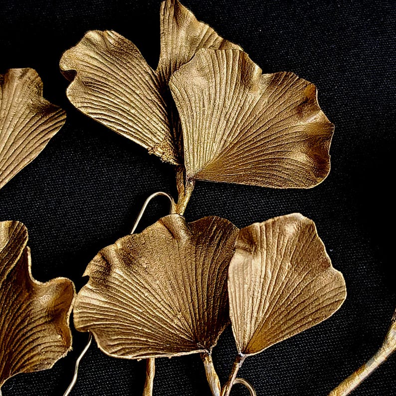 May include: A cluster of gold-painted ginkgo leaves arranged in a decorative pattern. The leaves are arranged in a fan-like shape, with the tips of the leaves pointing towards the center of the arrangement.