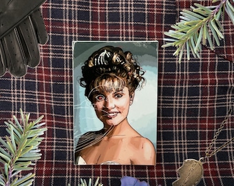 May include: An illustration of a woman with a red eye, a blue flower, a gold-colored broken heart pendant, and black leather gloves on a plaid background. The pendant says "FRIENDS".