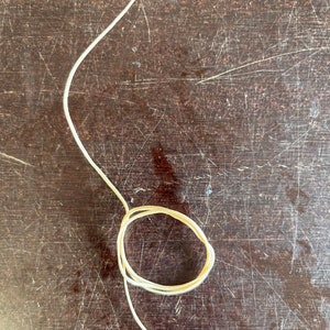 May include: A white cord is coiled into a circle on a brown wooden surface.