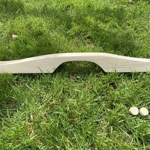 May include: A wooden bridge-shaped piece with two round wooden pieces on the grass.