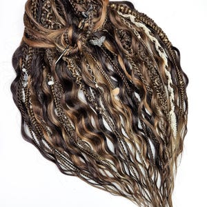 May include: A set of brown and blonde synthetic hair extensions featuring a mix of wavy strands, tight braids, and twisted sections. The hair is adorned with small metallic charms, beads, and a cream-colored lace ribbon woven throughout the texture.
