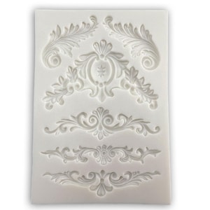 May include: White silicone mould with six different decorative designs. The designs are intricate and feature swirls, leaves, and flowers.