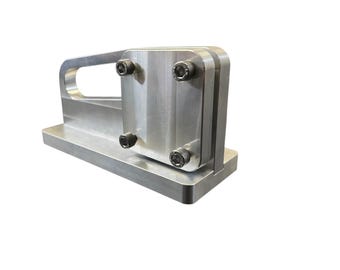 May include: A silver-colored metal object with a rectangular base, a vertical section, and a handle. Four black bolts secure the vertical section. The object appears to be a tool or a component of a larger machine.