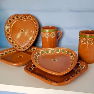 Puede incluir: Conjunto de cuatro platos de cerámica de terracota con diseños pintados en verde y blanco. Los platos incluyen un plato en forma de corazón, un plato cuadrado y dos tazas.