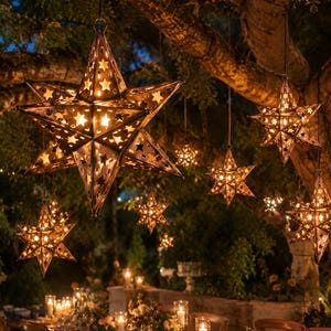 May include: Multiple hanging star-shaped lanterns made of dark metal with intricate star-shaped cutouts. Each lantern glows with warm internal light, suspended from tree branches above a long dining table set with candles and floral arrangements.