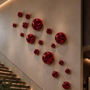 Puede incluir: Un interior moderno con una escalera y arte mural. La pared presenta una serie de esculturas murales esféricas rojas brillantes de varios tamaños. La escalera tiene escalones de madera y una barandilla de vidrio. El diseño es contemporáneo y artístico.