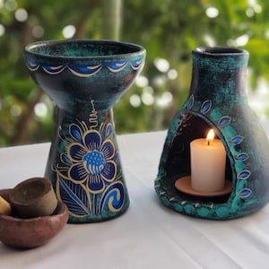 May include: Two teal blue ceramic incense burners with intricate floral designs. One burner has a small white candle burning inside. The other burner has a small bowl with incense sticks and charcoal.