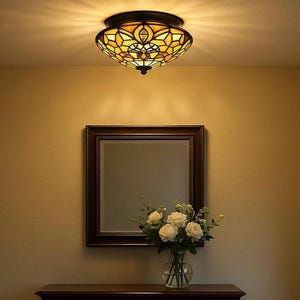 May include: A stained glass ceiling light fitting with a bronze finish. The light features a floral design in shades of yellow, orange, and brown. Below the light is a framed mirror and a vase of white roses.