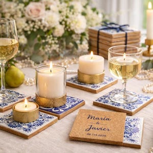 Puede incluir: Una mesa festiva con velas encendidas, copas de vino y posavasos decorativos. Los posavasos presentan un diseño de azulejos azules y blancos. Un posavasos de corcho muestra los nombres "Maria & Javier" y la fecha "06.115.2026".