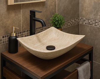 May include: A modern bathroom vanity with a square, beige stone sink. The sink sits on a dark wood cabinet with black metal framing. A black faucet, soap dispenser, and a small plant complete the setup. The background features brown tiles.