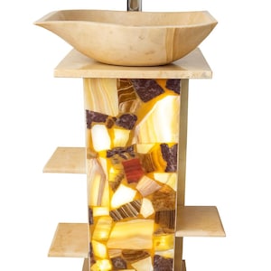 May include: A unique bathroom vanity with a beige stone vessel sink and a chrome faucet. The vanity base is a mosaic of amber, brown, and cream-colored stone pieces. Two small shelves are on the side of the vanity.