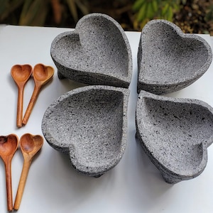 May include: Four gray heart-shaped bowls made of volcanic rock, arranged in a clover shape, with four wooden heart-shaped spoons.