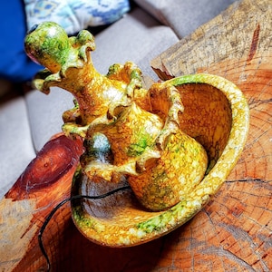 May include: A ceramic fountain with a multi-tiered design. The fountain is painted in shades of yellow, green, and brown, with a marbled effect. The fountain is sitting on a wooden surface.