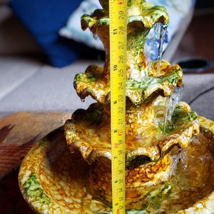 May include: A three-tiered ceramic fountain with a yellow, green, and brown glaze. The fountain is 30.5 cm tall and features a cascading water design.