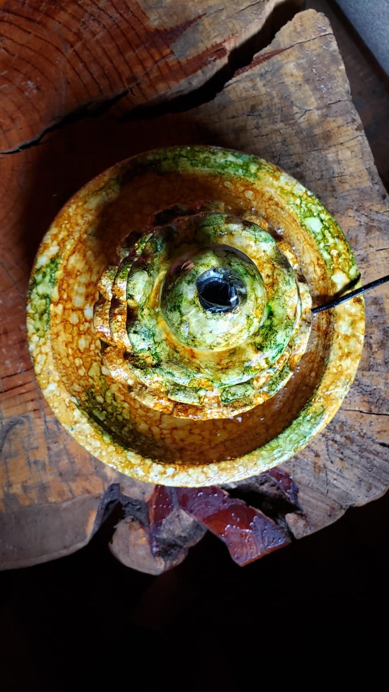May include: A ceramic fountain with three tiers, featuring a green and yellow glaze. The fountain has a round, open top and a small hole in the centre.