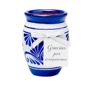 Puede incluir: Un jarrón de cerámica azul y blanco con un diseño floral decorativo. El jarrón tiene un borde azul y una cinta blanca atada alrededor. Una etiqueta blanca con las palabras "Gracias por acompañarnos" está adjunta.