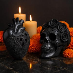 Puede incluir: Dos candelabros decorativos negros, uno en forma de corazón con recortes de estrellas, el otro con forma de calavera, ambos con diseños intrincados. Velas encendidas y flores naranjas crean un ambiente de Día de Muertos.