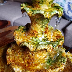 May include: A three-tiered tabletop fountain with a green and brown marbled finish. Water flows from the top tier down through the tiers, creating a relaxing sound.
