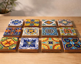 May include: A set of twelve square ceramic coasters with vibrant floral and geometric patterns. The coasters display a range of designs in blue, yellow, orange, and green, set on a wooden base. They are arranged on a light brown wooden surface, perfect for drinks.