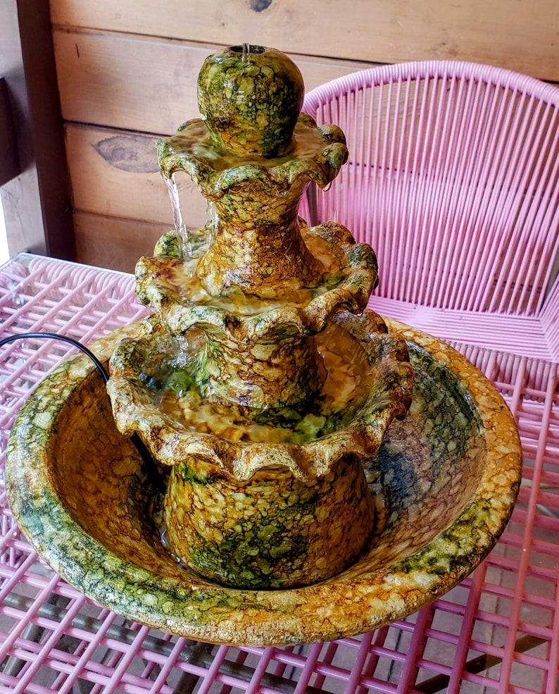 May include: A three-tiered ceramic fountain with a green and brown marbled design. Water flows from the top tier down to the bottom basin.