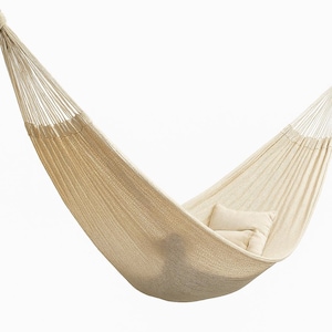 Puede incluir: Una hamaca beige con textura tejida, suspendida de cuerdas blancas. Dos almohadas a juego descansan en el interior. La hamaca está diseñada para la relajación y el uso al aire libre.